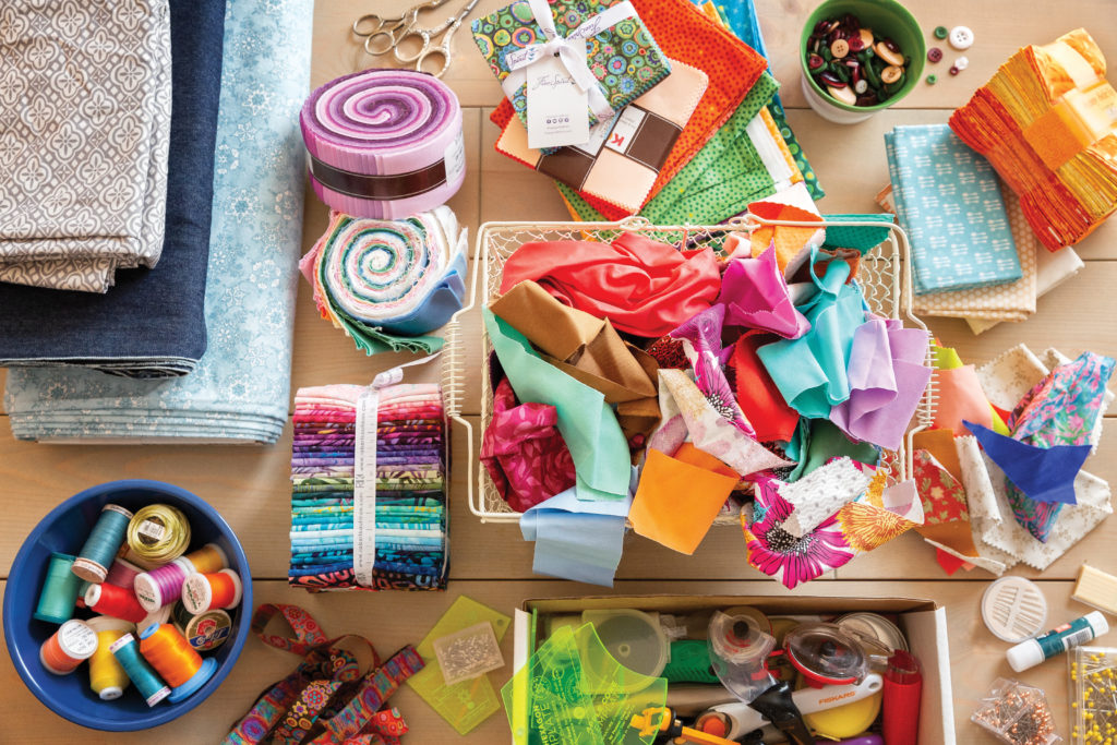 Quilt fabric, notions, buttons and more on a sewing room table. Find this image in BLOCK Magazine, Volume 7, Issue 1. 